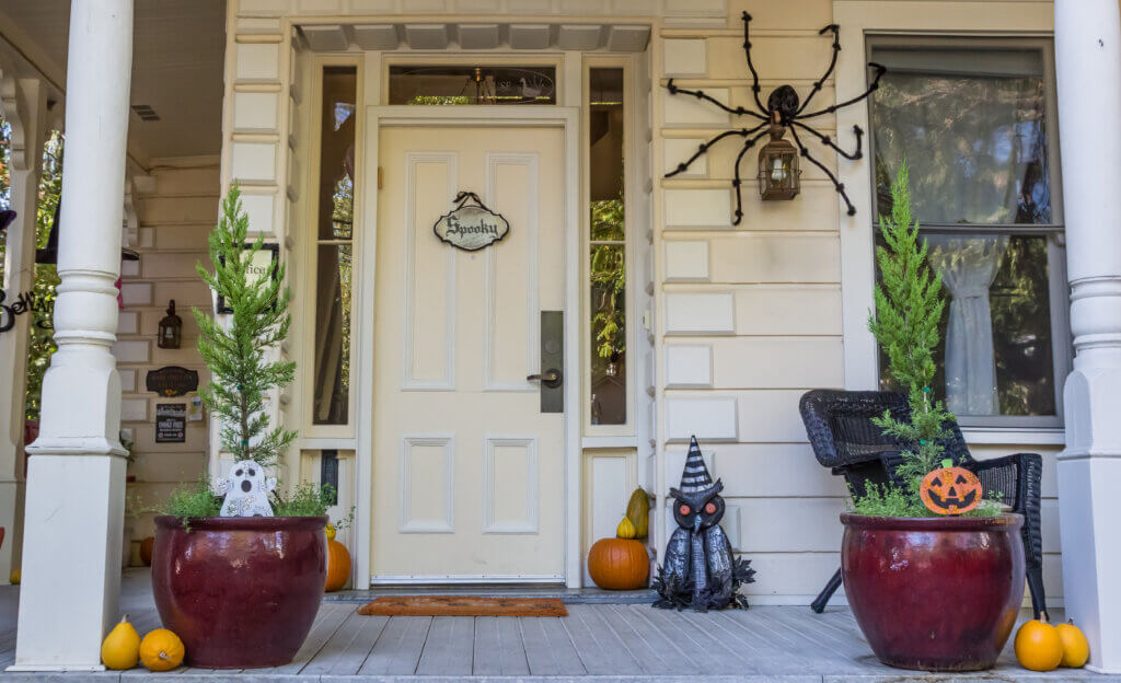 A porch decorated for Halloween with a Spooky sign, large spider, pumpkins, and themed ornaments.